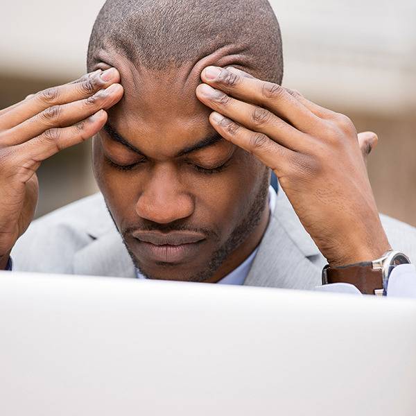 Stressed man in a suit sits at a desk, eyes closed—may benefit from natural pain relief for better focus.