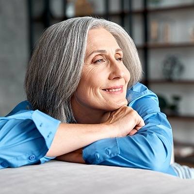 Older woman with gray hair in a blue shirt smiles and relaxes, considering natural pain relief options.