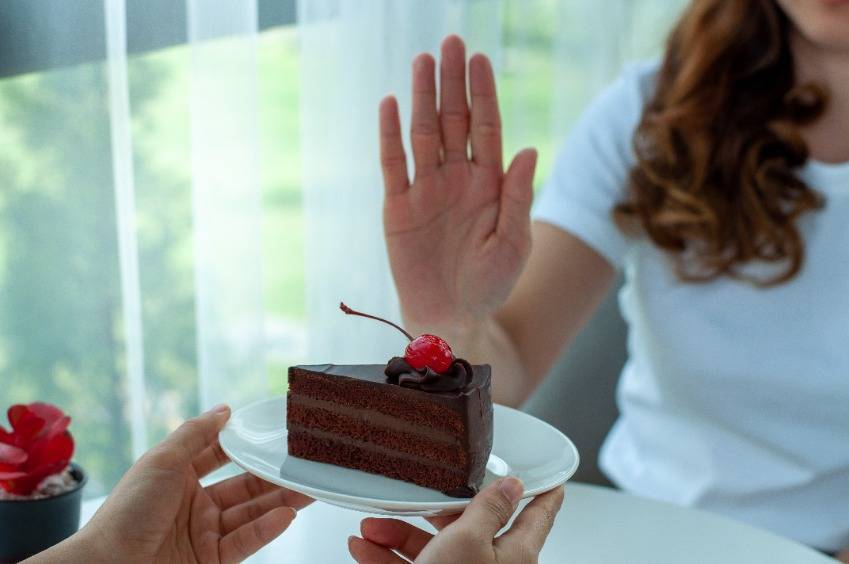 A person in a white shirt declines cake, choosing natural pain relief for a healthier lifestyle.
