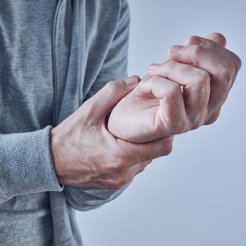 A person in a gray hoodie holds their left wrist, possibly seeking relief from discomfort with natural remedies.