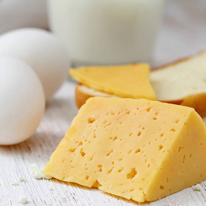 A wedge of yellow cheese with eggs, bread, and milk beside it—great for a balanced breakfast.