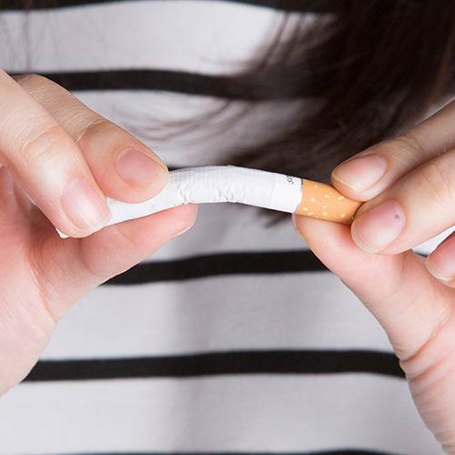 A person in a striped shirt bends a cigarette with both hands, possibly thinking about healthier lifestyle choices.