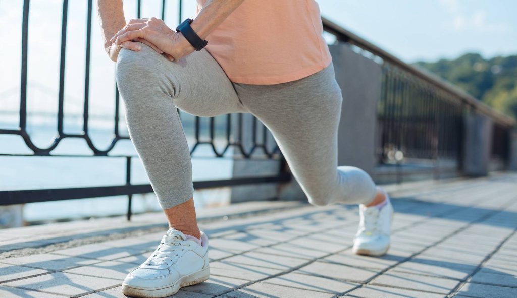 Person in gray leggings and white sneakers doing a lunge stretch, with natural pain relief supplements nearby.