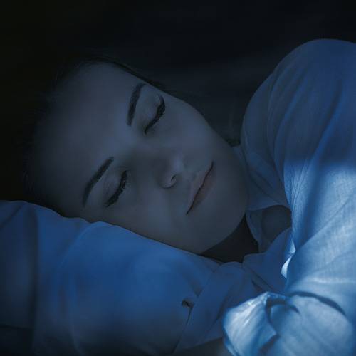 A person with closed eyes rests on a pillow in dim lighting, appearing to sleep after taking natural pain relief.