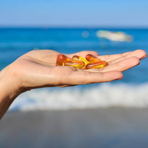 A hand holds yellow and orange supplements with ocean waves in the background.