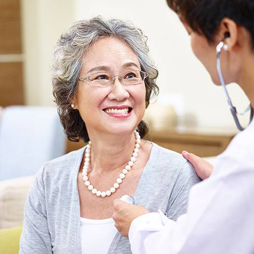 An older woman smiles as a healthcare professional listens to her chest and discusses natural pain relief options.