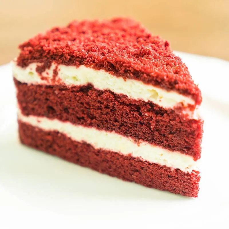 Red velvet cake slice with two layers of cream cheese frosting, next to supplements on a white plate.
