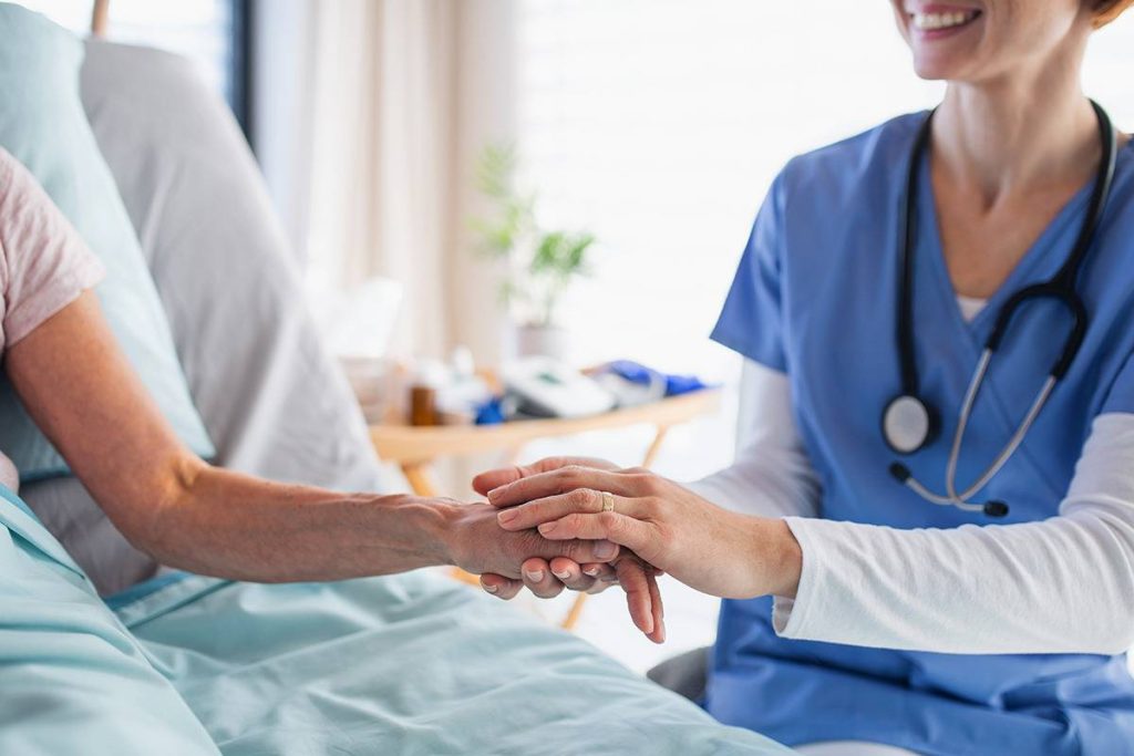 A nurse in blue scrubs comforts a patient, discussing natural supplements for added hospital support.